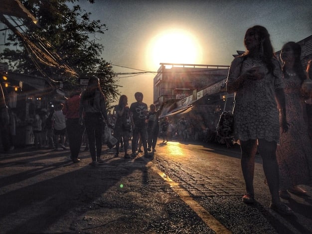 A still from a Latin American crime drama depicting a scene in a crowded favela or barrio, where residents are shown struggling with poverty and lack of access to basic services. Graffiti and street art adorn the buildings, reflecting the vibrant yet challenging environment.