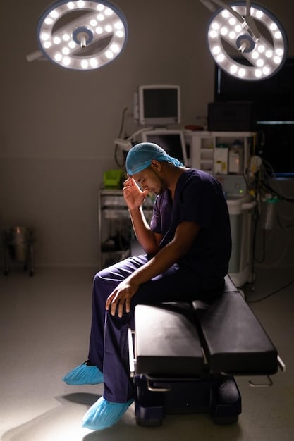 A doctor sits alone in a dimly lit office, head in hands, appearing exhausted and burdened by the weight of their decisions.